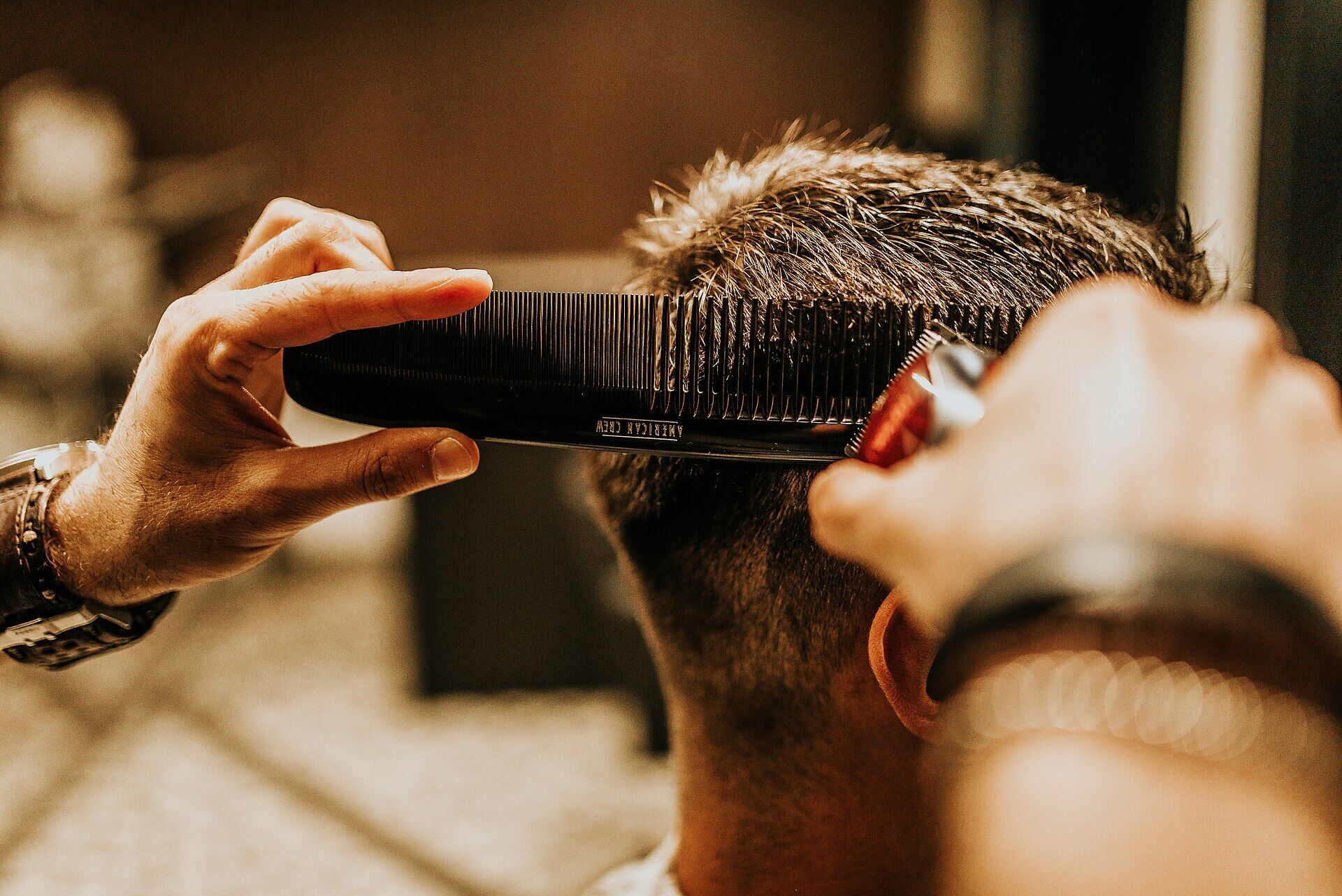 A barber cutting a customer's hair with clippers and a comb