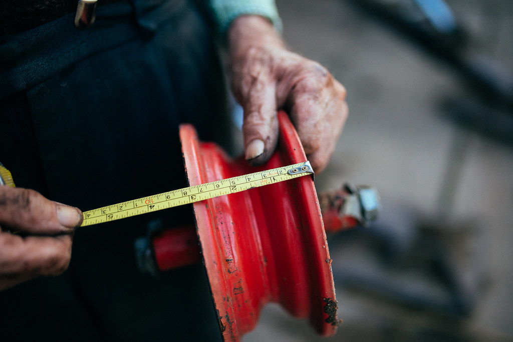 A craftsman measuring a metal wheel with a tape measure